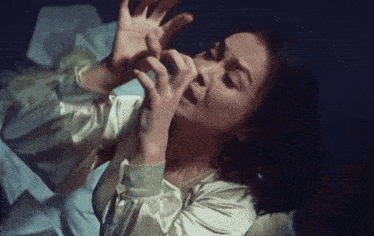 a woman in a white dress is laying in bed with her hands on her face