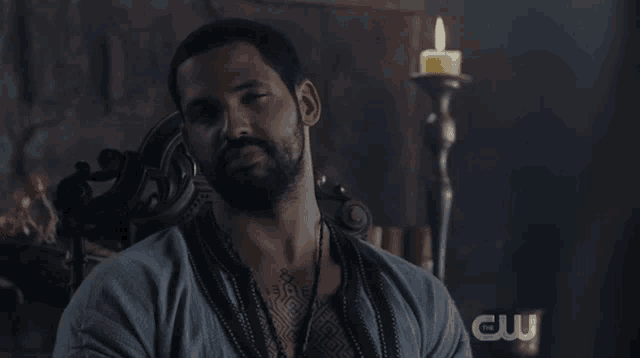a man with a tattoo on his chest is sitting in front of a candle and a cw logo