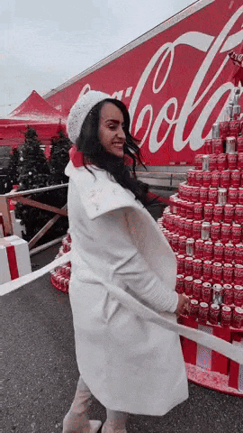 a woman in a white coat is standing in front of a large coca cola truck .