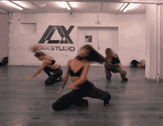 a group of women are dancing in front of a wall that says axstudio
