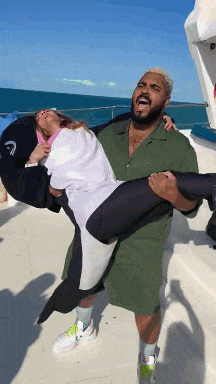 a man is carrying a woman in his arms on a boat in the ocean