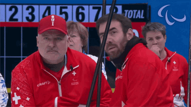 a group of people sitting in front of a scoreboard which says total