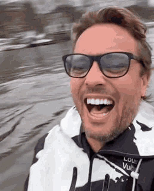 a man wearing sunglasses and a life vest is laughing with his mouth open .