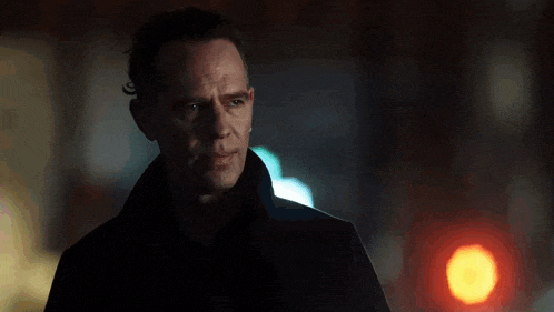a man in a black coat is standing in the dark looking at the camera .
