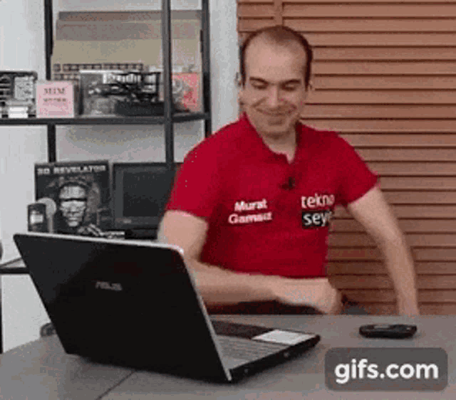 a man in a red shirt is sitting at a desk with a laptop