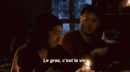 two men are sitting at a table and one of them is talking in french .