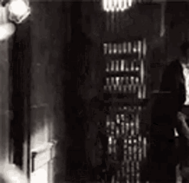 a black and white photo of a man in a suit standing next to a shelf .