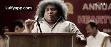 a man with curly hair is standing at a podium giving a speech in front of a microphone .