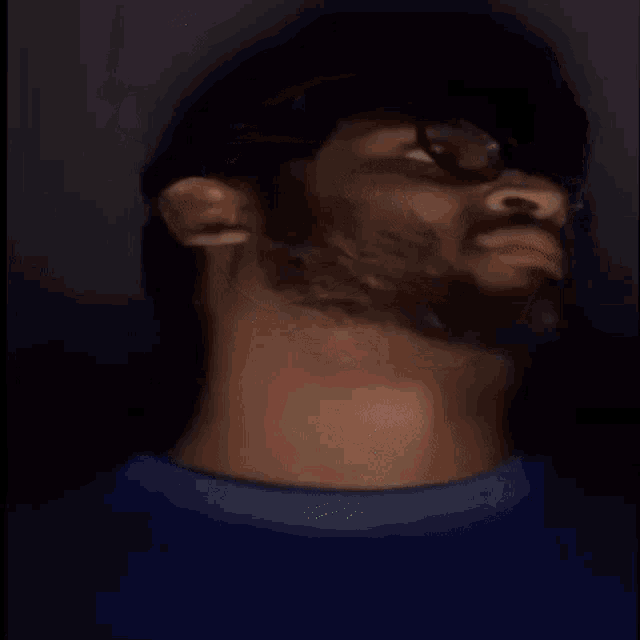 a man with glasses and a beard is making a funny face in the dark .