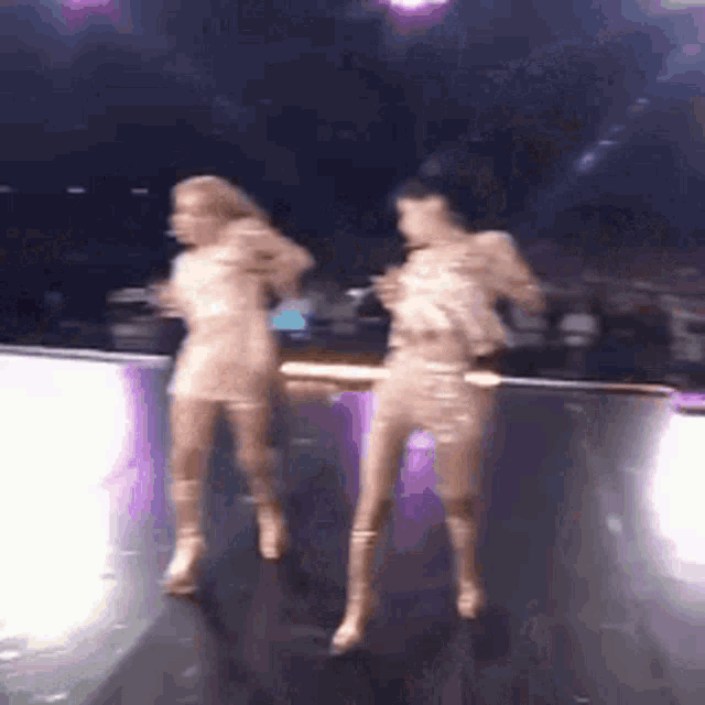 a couple of women are dancing on a stage in a dark room .