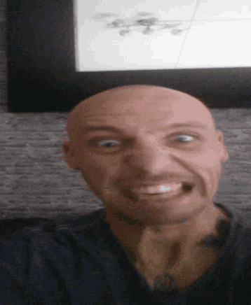 a bald man is making a funny face in front of a framed picture