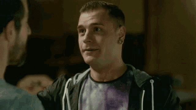 a man in a galaxy shirt is smiling at another man .