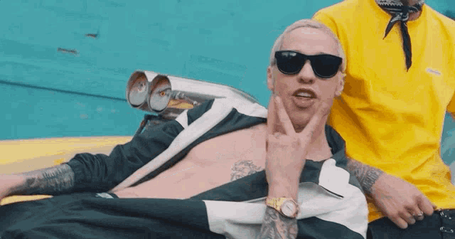 a man wearing sunglasses and a watch is laying on a yellow vehicle