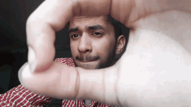 a man in a plaid shirt is making a heart shape with his fingers