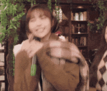a woman in a brown jacket is holding a microphone and smiling while standing in front of a bookshelf .