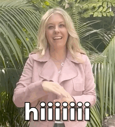 a woman in a pink jacket is standing in front of palm trees and making a funny face .