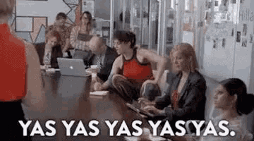 a group of people are sitting around a table with laptops and a sign that says yas yas yas yas .