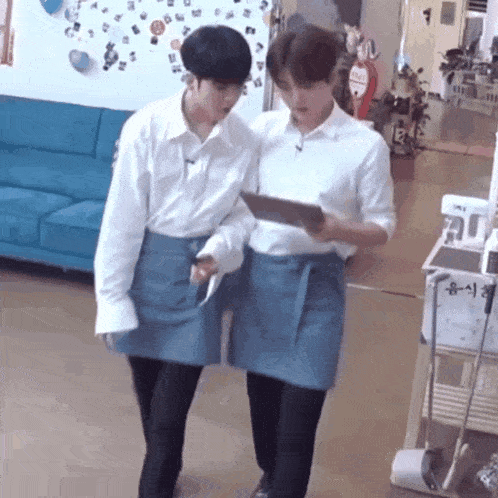 two men in aprons are standing next to each other in a living room .