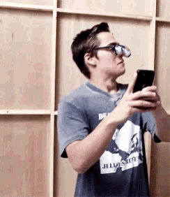 a man wearing glasses and a shirt that says jelly 's wife is looking at his phone