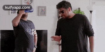two men are standing next to each other in a living room drinking water .