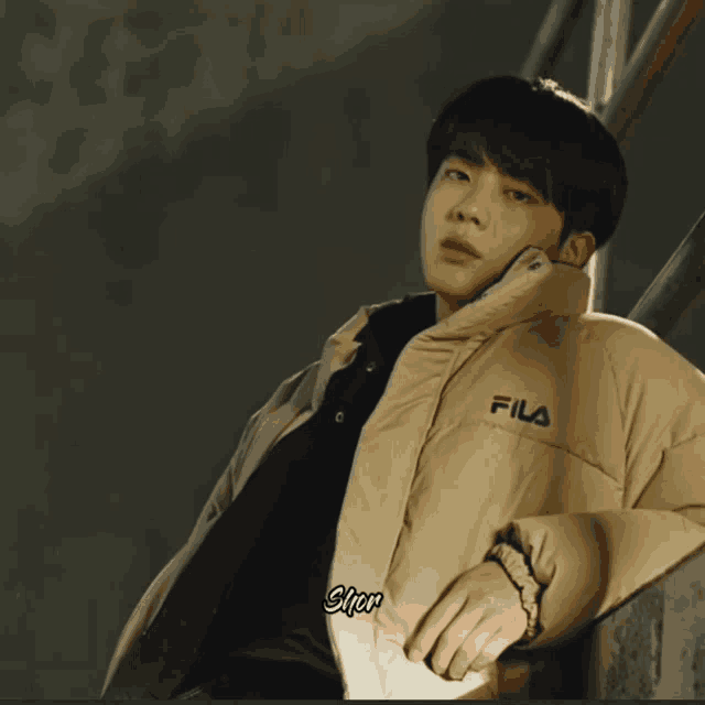 a man wearing a fila jacket is leaning against a wall