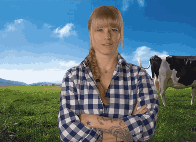 a woman in a plaid shirt stands in a field with her arms crossed in front of a cow