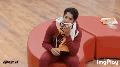 a man in a red jacket is sitting on a red cushion with a shocklat logo in the background