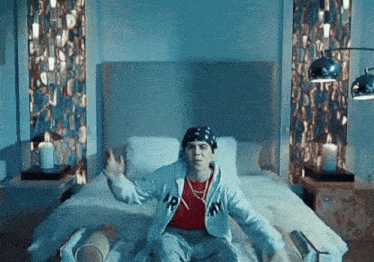 a man sitting on a bed wearing a hoodie with the letter n on it