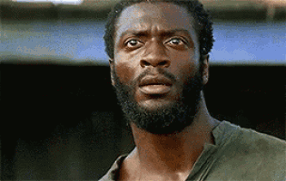 a man with a beard and a green shirt is looking at the camera with a surprised look on his face .