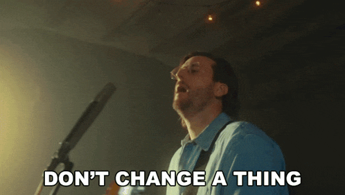 a man singing into a microphone with the words " do n't change a thing " behind him