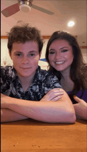 a man and a woman are posing for a picture with a ceiling fan behind them