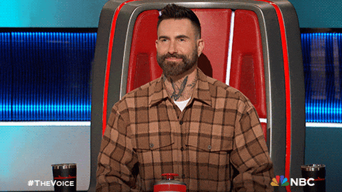 a man in a plaid shirt is sitting in a chair with a nbc logo on the back