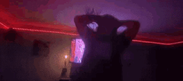 a man is sitting in front of a television in a dark room with red and blue lights .