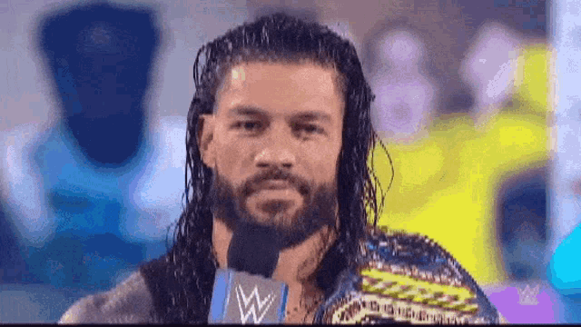 roman reigns is wearing a wrestling championship belt while talking into a microphone .