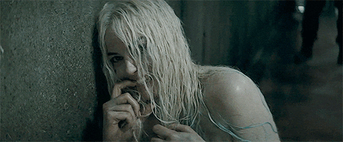 a woman with blonde hair is leaning against a wall and biting her nails .