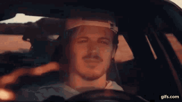 a man wearing a hat is driving a car and looking out the window .