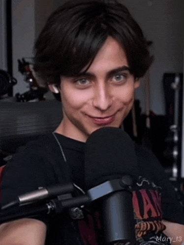 a young man is smiling in front of a microphone while wearing a black shirt .