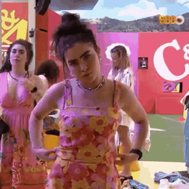 a woman in a floral dress is standing with her hands on her hips in front of a group of women .