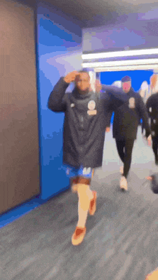 a group of people are walking down a hallway and one of them is wearing a black jacket with the letter s on it .