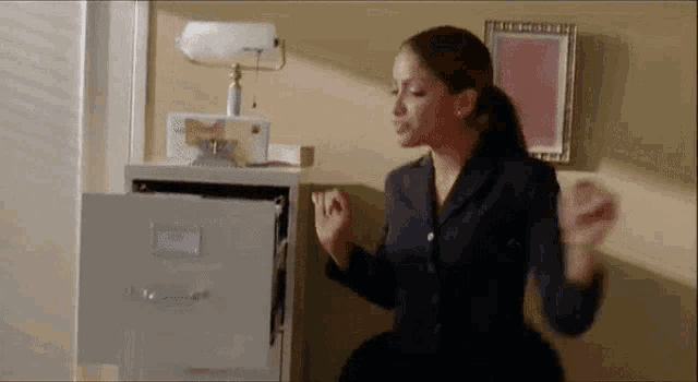 a woman is sitting in front of a filing cabinet with the door open .