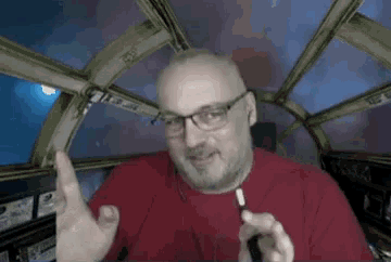 a bald man wearing glasses and a red shirt is sitting in a space ship .