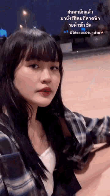 a girl wearing a plaid shirt and a white tank top looks at the camera