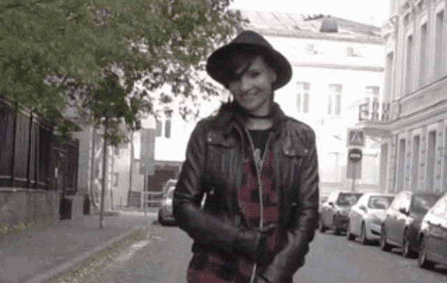 a woman wearing a black hat and a leather jacket stands on a street