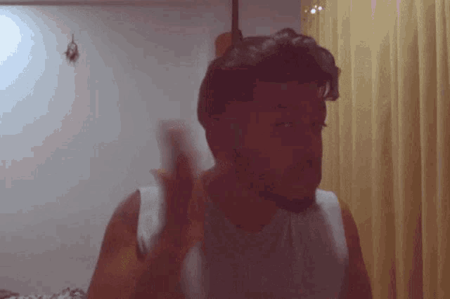 a man with a beard wearing a white tank top is waving his hand