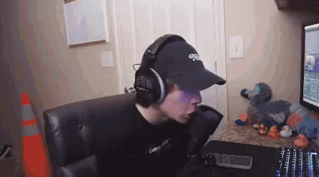 a man wearing headphones and a baseball cap is sitting in front of a computer .