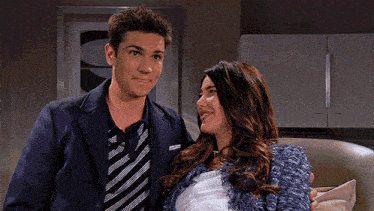 a man in a suit and tie stands next to a pregnant woman in a blue jacket