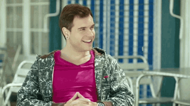 a young man wearing a pink shirt and a gray jacket is smiling
