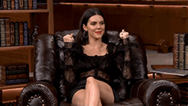 a woman in a black dress is sitting in a leather chair