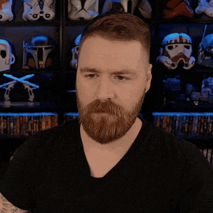 a man with a beard wearing a black shirt stands in front of a shelf full of stormtrooper helmets