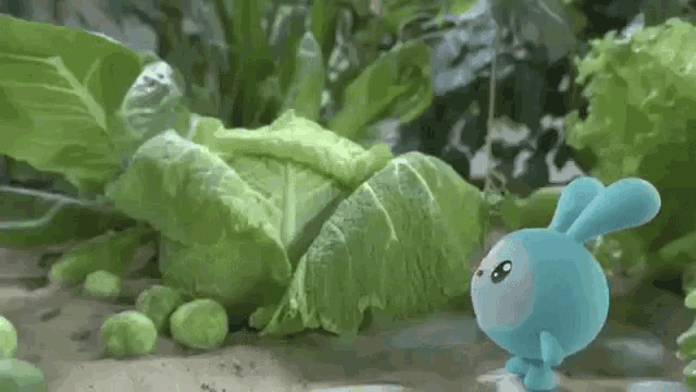 a blue rabbit is standing in front of a bunch of green vegetables .